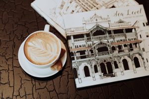 A latte with a delicate foam art rests on a saucer beside a biscotti, capturing the essence of caffeine and culture against the backdrop of a sketchbook with architectural drawings, evoking a sense of creative inspiration and tradition.